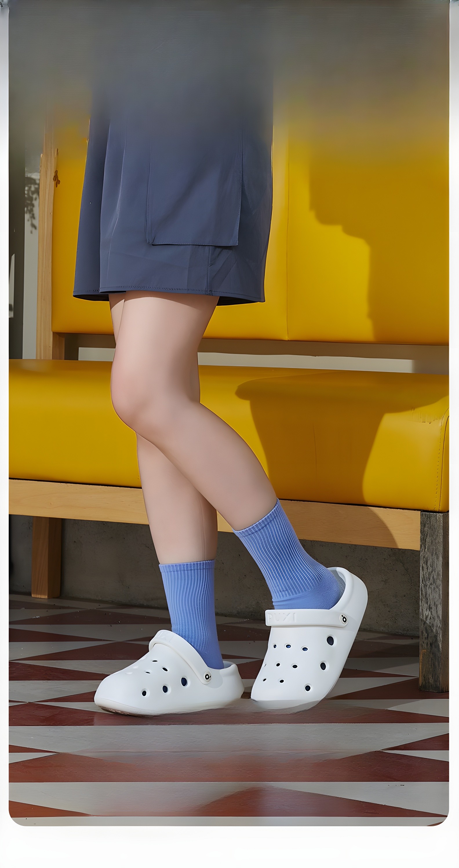Person walking in white PUXI sandals near a yellow bench, showing the sandals in motion and in a vibrant setting