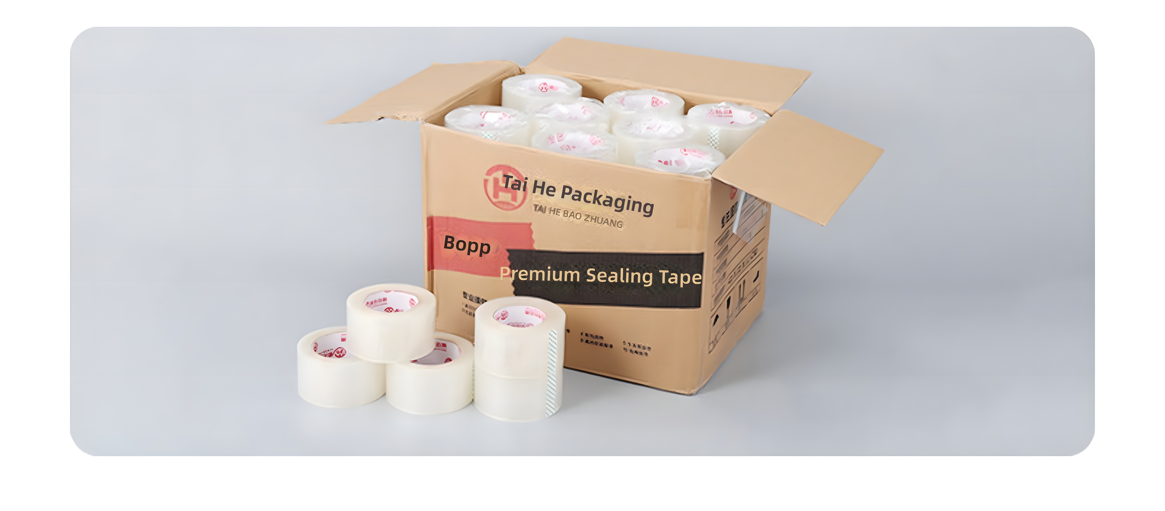 Color product shot: open brown cardboard carton labeled 'Tai He Packaging Premium Sealing Tape' with rolls inside and 4 rolls in foreground