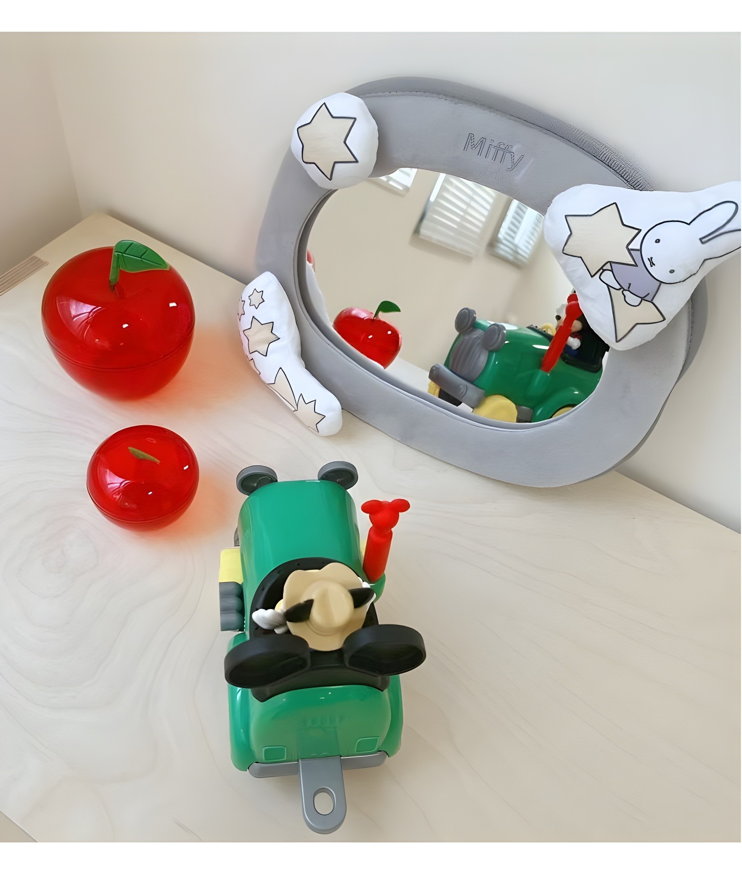 Close-up of grey Miffy mirror with red apple toys and green toy car in foreground