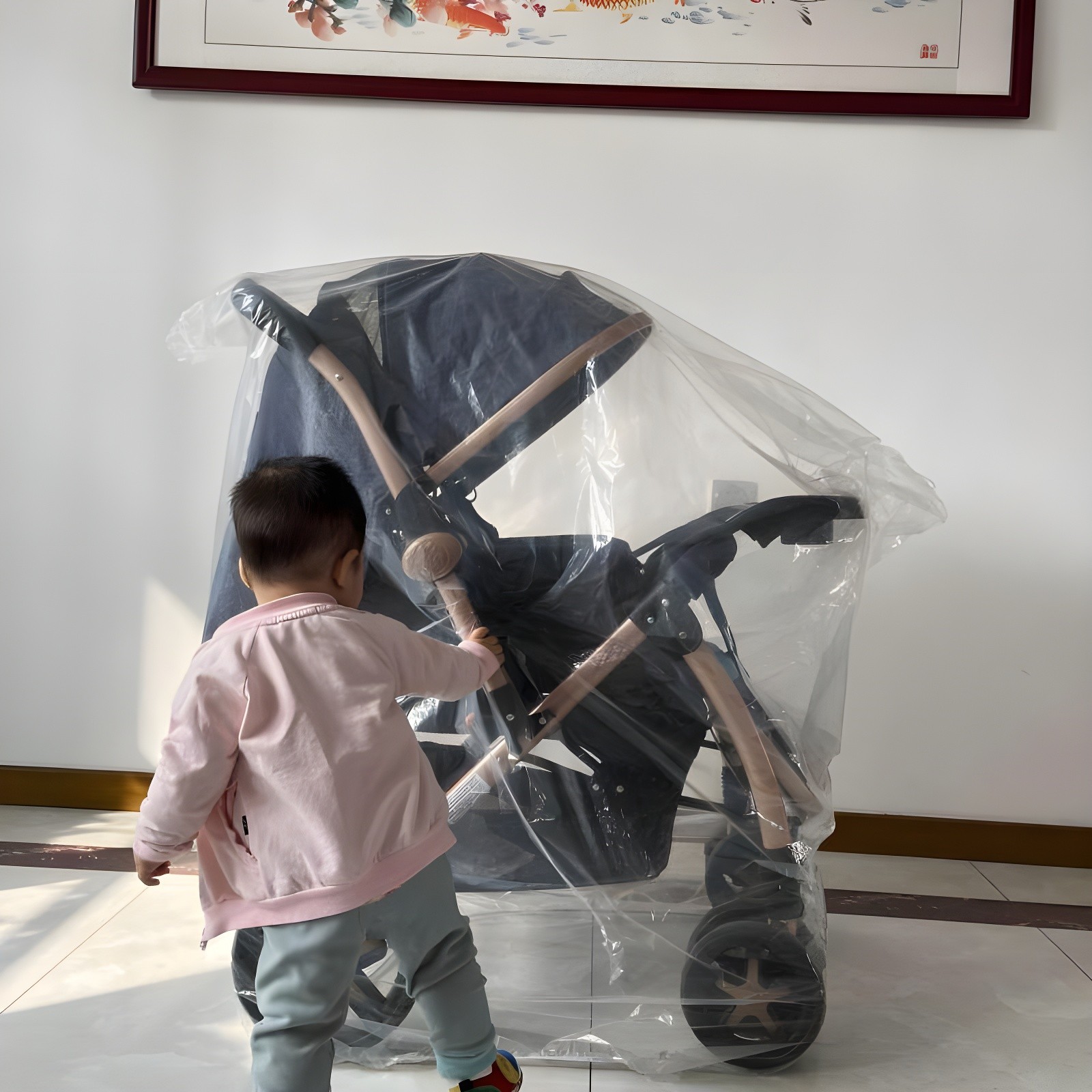 Toddler in pink jacket approaching and touching the wrapped Aurora stroller, symbolizing early connection and discovery