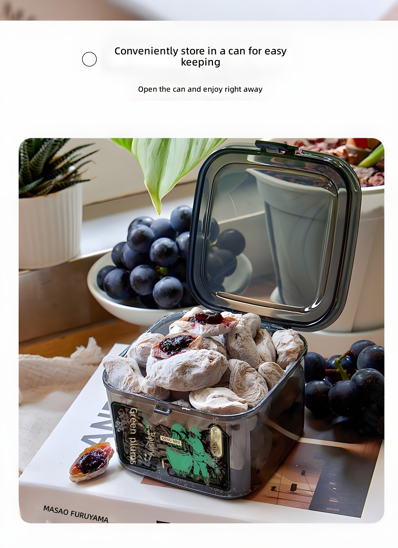 Color photo: an open transparent container filled with Qingmei Hug Bok Choy pieces, placed on a book next to fresh black grapes and a potted succulent. One piece is broken open beside the container, revealing the dark jam filling.