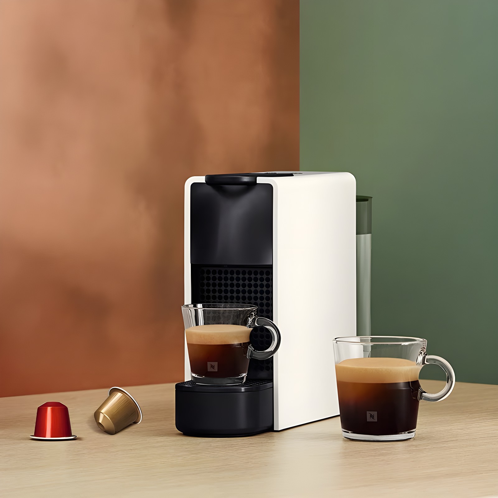 White Nespresso Essenza Mini on wooden table with two espresso cups and capsules