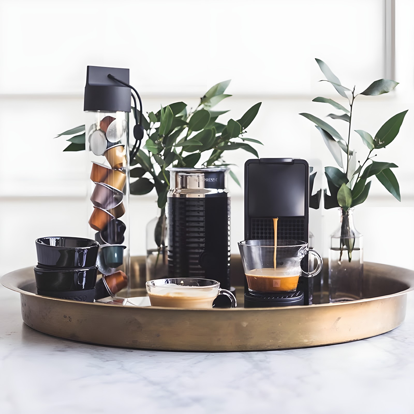Black Nespresso Essenza Mini on brass tray with milk frother, capsules, and greenery